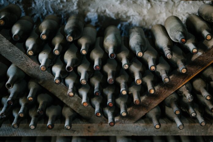 From above of dusty bottles of alcohol drink placed above each other in rows in winery