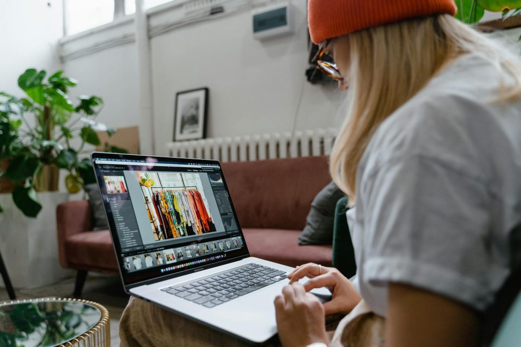 Woman using a laptop for photo editing in a cozy, plant-filled living room setting.