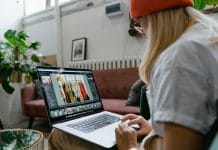 Woman using a laptop for photo editing in a cozy, plant-filled living room setting.