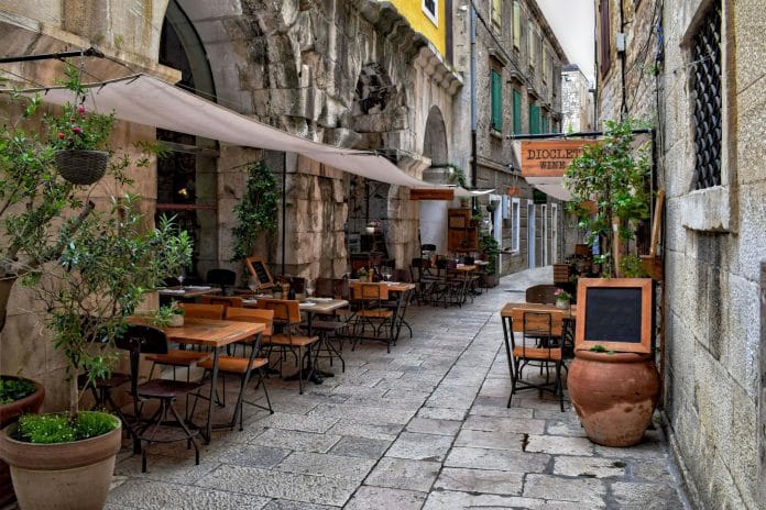 Cozy narrow alley in Croatia with charming outdoor cafe seating in historic setting.