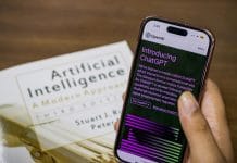 Close-up of a smartphone displaying ChatGPT app held over AI textbook.