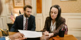 How US law firms get more clients from directories Three professionals exchange legal documents during a formal meeting at a conference table, representing client acquisition strategies for law firms.