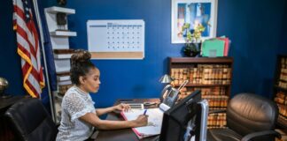 How to optimize a US lawyer directory profile in 2026 Attorney working at desk with computer monitor and legal books in office with American flag, representing professional environment for optimizing lawyer directory profiles.