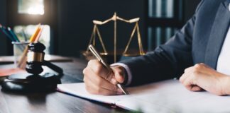 Alaska web directory of law firms Attorney in navy suit writes at wooden desk with gavel and scales of justice, representing professional legal practices featured in Alaska law firm directories.