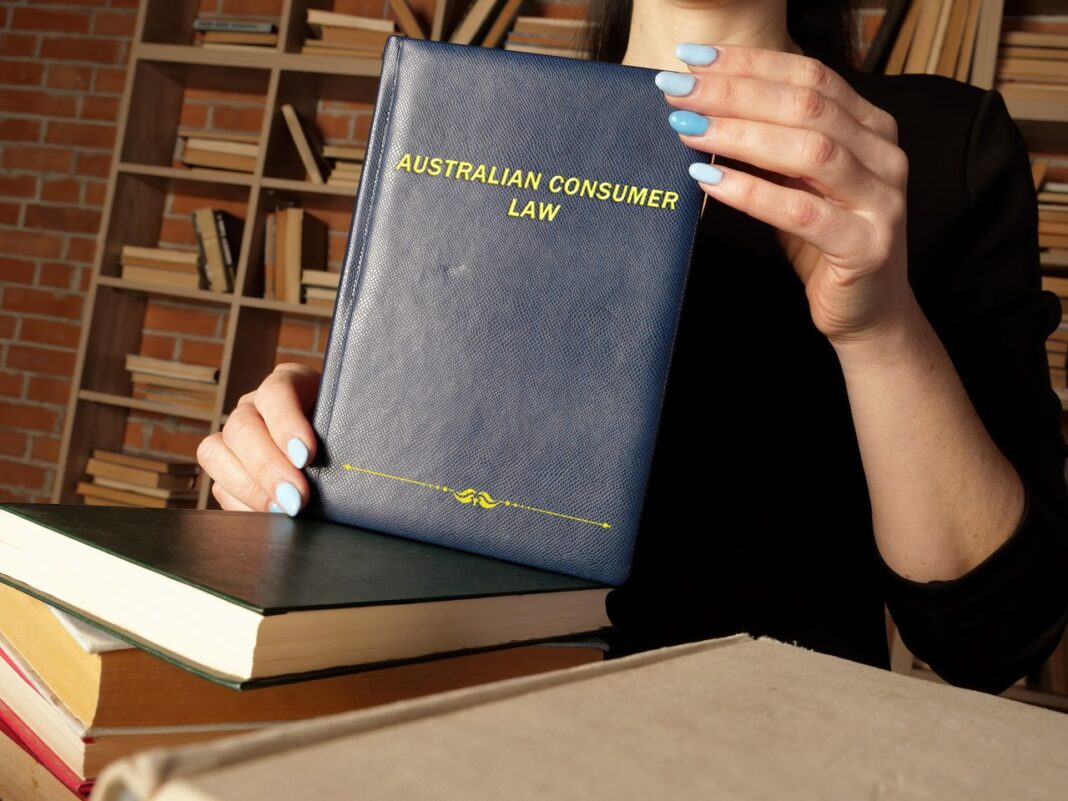 Australian Consumer Law book representing legal resources and directories for professional reference Person holding Australian Consumer Law hardcover book with gold lettering against a bookshelf background, illustrating legal reference materials used in professional law firm directories.