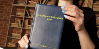 The best law firm directories in Australia for 2026 Person holding Australian Consumer Law hardcover book with gold lettering against a bookshelf background, illustrating legal reference materials used in professional law firm directories.