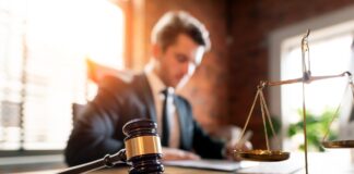 Why New Jersey lawyers use a law firm directory in 2026 Wooden gavel and brass scales of justice on a desk with a lawyer working at a computer in the background, representing modern legal practice and professional directories.