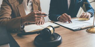 Two professionals review legal documents at a table with gavel and scales of justice, representing attorney consultations available through legal directories.