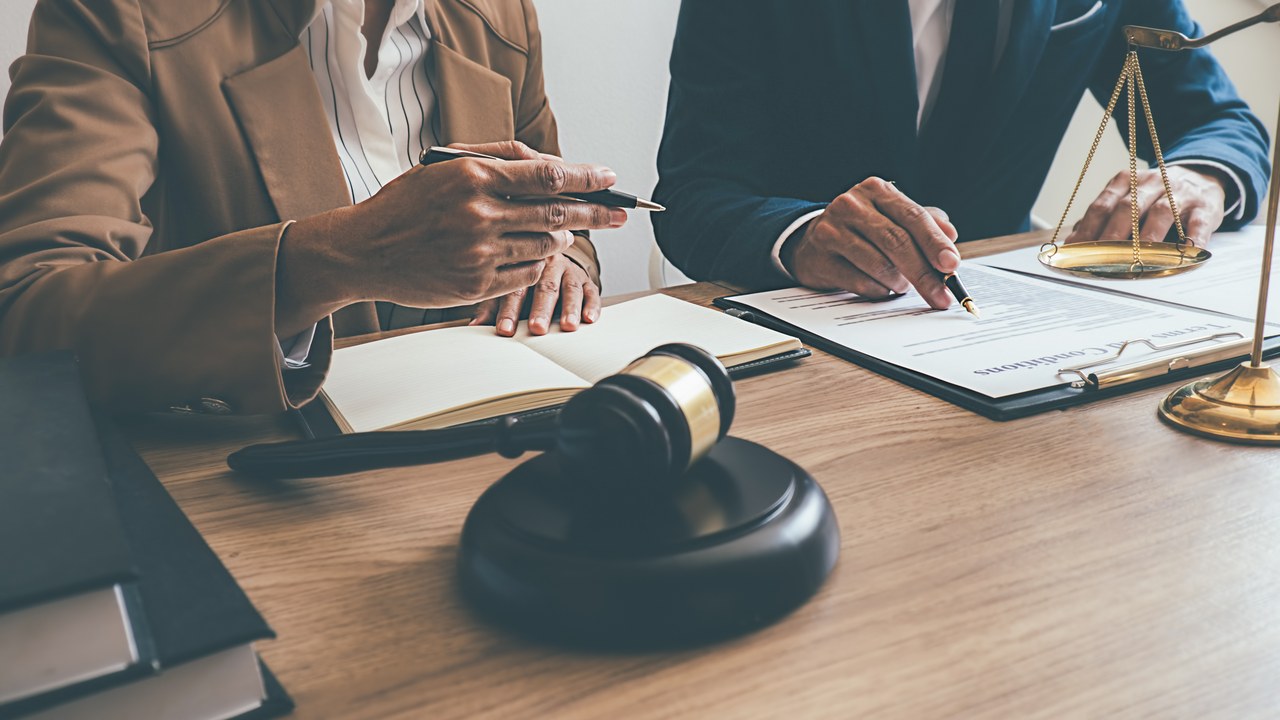 Two professionals review legal documents at a table with gavel and scales of justice, representing attorney consultations available through legal directories.