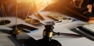 Wooden gavel and brass balance scale on office desk with papers and calculator, representing the careful evaluation lawyers undertake when choosing professional directories.