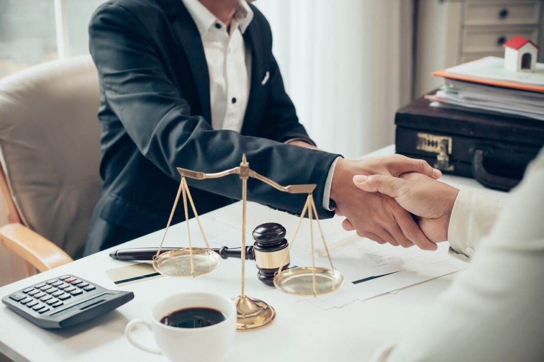 Professional legal consultation handshake illustrating client-lawyer connections through Australian law firm directories Two business professionals shake hands across a desk with legal symbols including scales of justice and gavel, representing connections made through law firm directories.