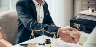 How legal directories refer clients to AU law firms Two business professionals shake hands across a desk with legal symbols including scales of justice and gavel, representing connections made through law firm directories.