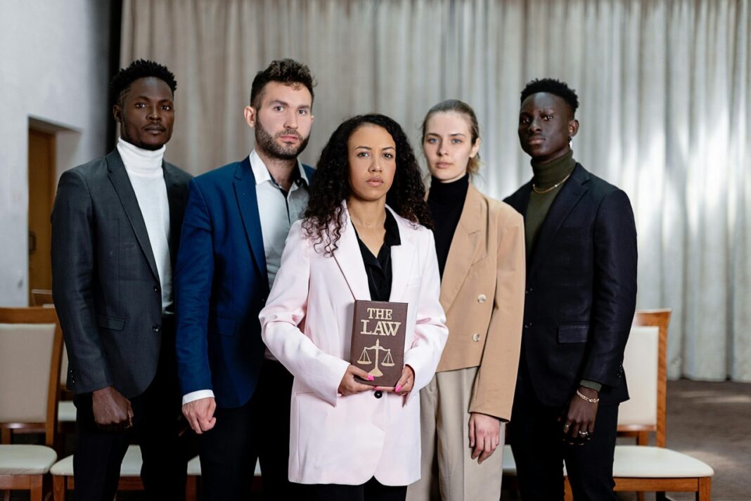 Professional legal team portrait illustrating solo lawyer practice and legal directory presence Five professionally dressed people stand together as one holds a law book with scales of justice, representing legal professionals in independent practice.