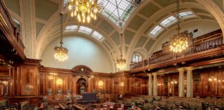 Ornate legislative chamber with tiered semicircular seating, chandeliers, and wood paneling, representing government institutional spaces included in official directories.