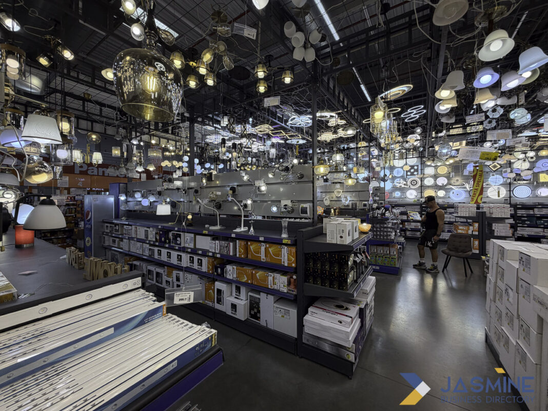 Overwhelming choice in lighting showroom illustrates the challenge of selecting quality over quantity in business decisions. Hundreds of lighting fixtures hang from warehouse ceiling above organized shelving and a lone shopper, illustrating the overwhelming abundance that requires selective, quality-focused decision-making.