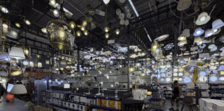 Quality over quantity: how many directories to submit to Hundreds of lighting fixtures hang from warehouse ceiling above organized shelving and a lone shopper, illustrating the overwhelming abundance that requires selective, quality-focused decision-making.