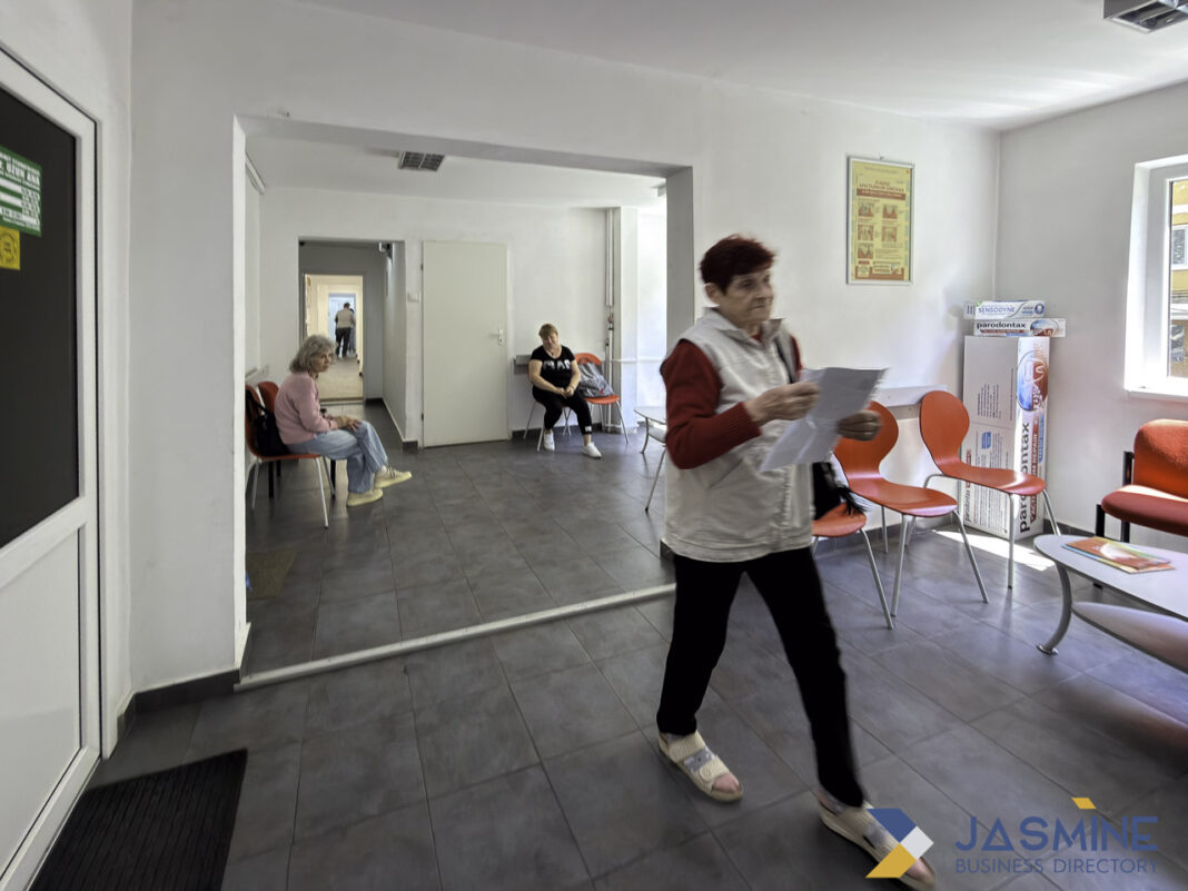 Medical clinic waiting room interior illustrating healthcare access and physician directory navigation A medical clinic waiting room with orange chairs and motion-blurred patient holding paperwork, representing healthcare accessibility and physician directory navigation.