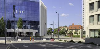 Modern glass office building at an urban street intersection with traffic markings and traditional buildings, representing the professional commercial environment of metropolitan legal services.