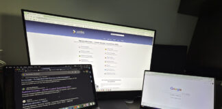 Three-screen workspace with laptops and monitor displaying business directory pages, illustrating the digital tools used to create and manage online business listings.