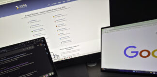 Three laptop screens on a desk display business directory and search engine interfaces, illustrating the comparison between directory listings and paid advertising platforms.