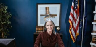 Professional woman seated at wooden desk in formal office with American flag and law books, illustrating authority and credibility for law firm directory selection.