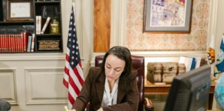 List your firm in the New Hampshire law firm directory Professional woman in pinstripe suit working at traditional office desk with American flag, representing attorneys listing their firms in legal directories.