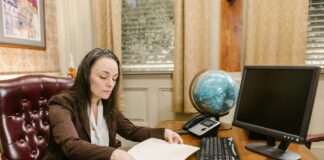 How to optimise a UK lawyer directory profile for 2026 A professional woman reviews documents at her office desk with computer monitor and keyboard, representing the workspace of lawyers managing their online directory profiles.