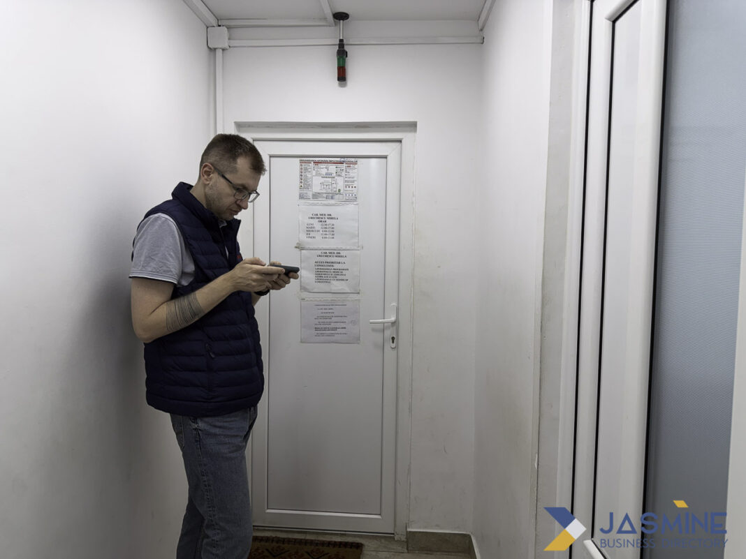 Service professional checks mobile device illustrating how trade businesses use digital directories in 2026 Service professional in navy vest checks mobile phone in industrial corridor, representing how trade businesses access digital directories for customer connections.