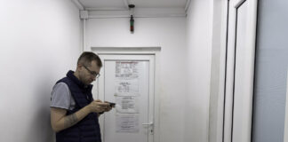 Service professional in navy vest checks mobile phone in industrial corridor, representing how trade businesses access digital directories for customer connections.