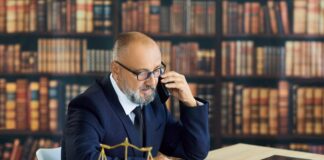 How legal directories bring cases to UK law firms Solicitor in navy suit speaks on phone at desk with scales of justice and law books, representing client consultation through legal directory referrals.