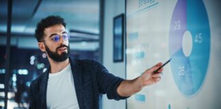 How Generative AI is Transforming Data Management for Business Listings Business professional in glasses gestures toward projected pie chart with statistics in modern office, illustrating data-driven approaches to business listing management.