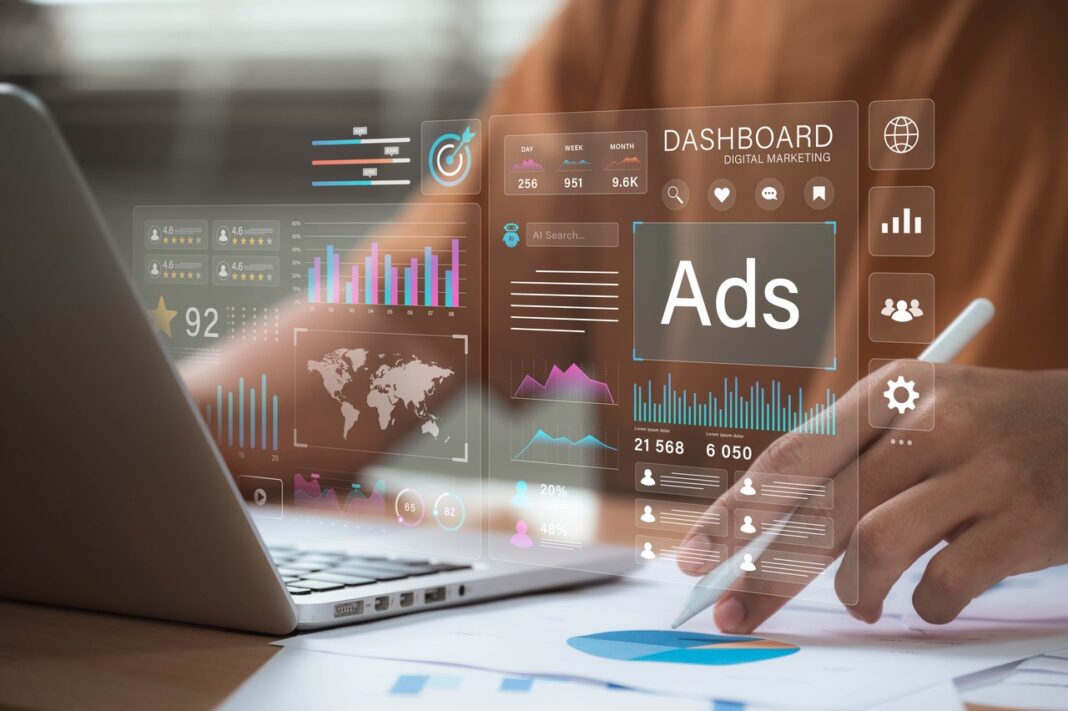 Modern marketing dashboard interface illustrating tools and analytics for the agentic web era Hands with stylus positioned over laptop workspace while transparent marketing dashboard overlay shows analytics charts and metrics, representing modern marketing technology tools.