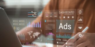 Future-Proofing Your Marketing Stack: Tools for the Agentic Web Hands with stylus positioned over laptop workspace while transparent marketing dashboard overlay shows analytics charts and metrics, representing modern marketing technology tools.