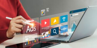 Person working on tablet with stylus while laptop sits nearby, holographic advertising and analytics icons floating above the workspace, illustrating content creation for AI-driven directory platforms.