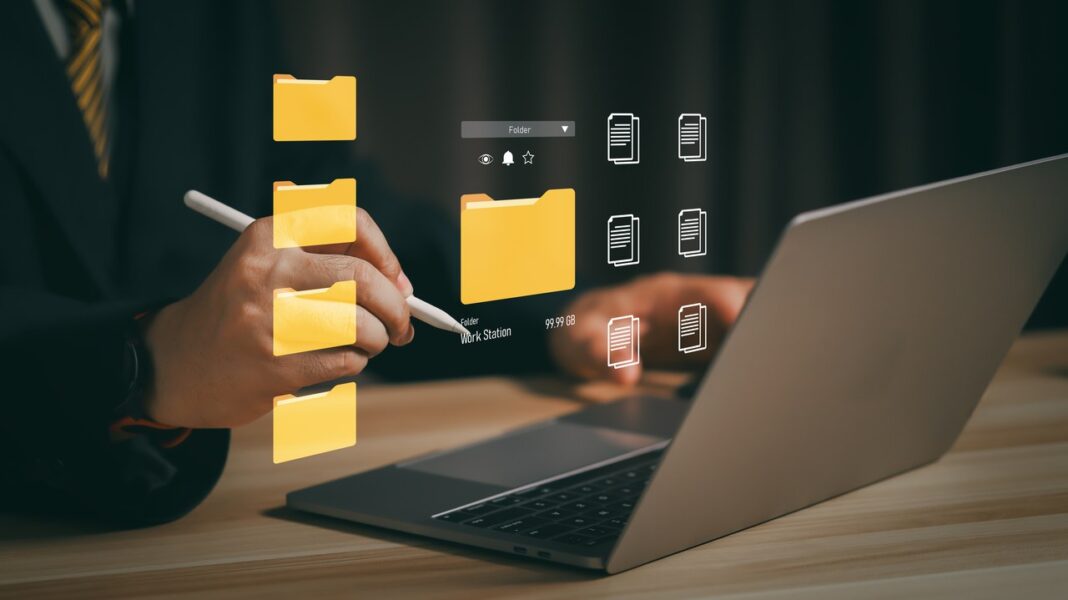Digital file organization concept illustrating AI-driven data cleaning and directory automation workflows Person working on laptop with digital folder and document icons overlaid, representing automated directory management and data organization systems for business workflows.