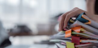 The Ultimate List of Free Directories Hand reaching toward tall stack of colorful folders and binders on office desk, illustrating the comprehensive collection of organized directory resources.