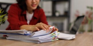 The Modern Role of Web Directories Office worker in red blazer organizing stacked paper documents with colored tabs at wooden desk, representing systematic categorization methods used in web directories.