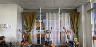 Orange and black agricultural tillers displayed in a showroom with glass partitions and curtains, illustrating retail product presentation for local business discovery.