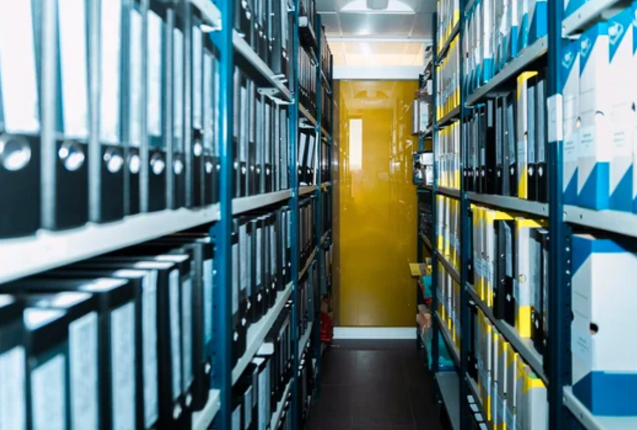 Corridor lined with metal shelves holding organized black binders in an archive facility, representing the systematic organization central to curated directory standards.