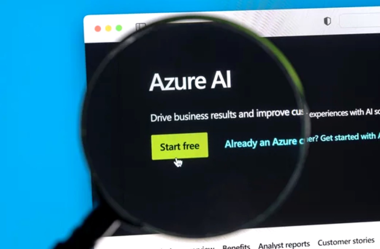 Magnifying glass hovering over a computer screen displaying Microsoft Azure AI website with yellow call-to-action button, illustrating examination of AI platform trends and infrastructure.