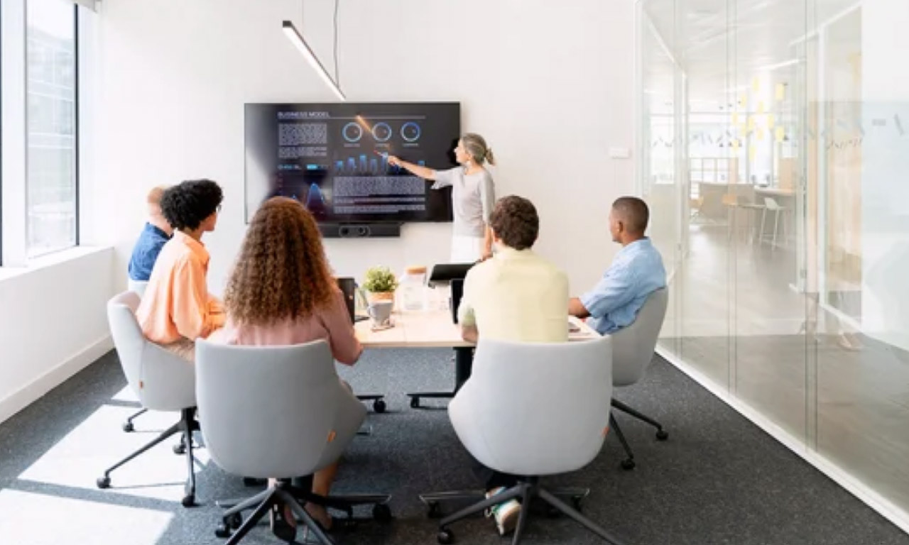 Business professionals in a modern conference room viewing analytics on a wall display, representing how contemporary business directories organize and present searchable company information.