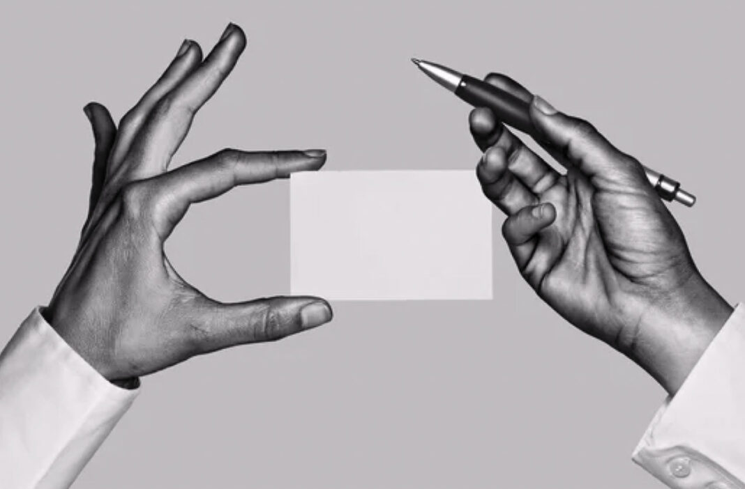 Professional business card exchange illustrates traditional marketing communication methods Two hands exchange a blank business card with a pen in a professional black and white photograph, representing traditional business marketing communication.