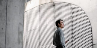A business professional in grey shirt stands in profile within a modern minimalist space with perforated wall panels, representing contemporary business identity and establishment.