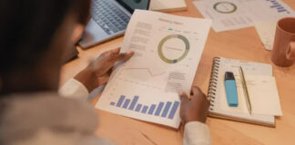 Person reviewing a marketing report with charts and graphs at a desk with laptop, illustrating business data analysis and source verification practices.