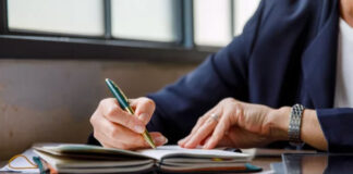 Close-up of hands in business attire writing with a gold pen in a notebook at a wooden desk, illustrating the planning process for creating dual-audience content.