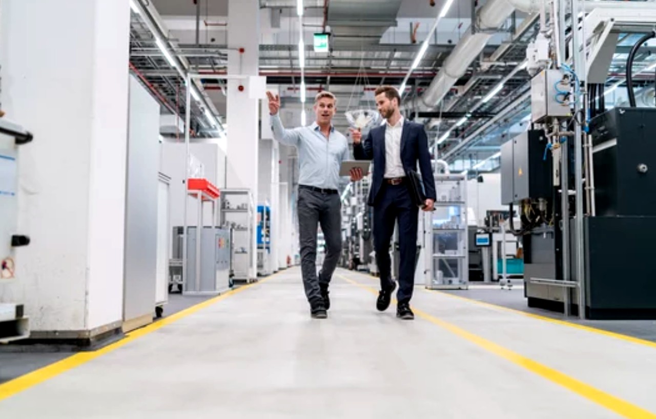 Two businessmen walking through a modern manufacturing facility with industrial machinery, illustrating contemporary approaches to B2B advertising in technical industries.