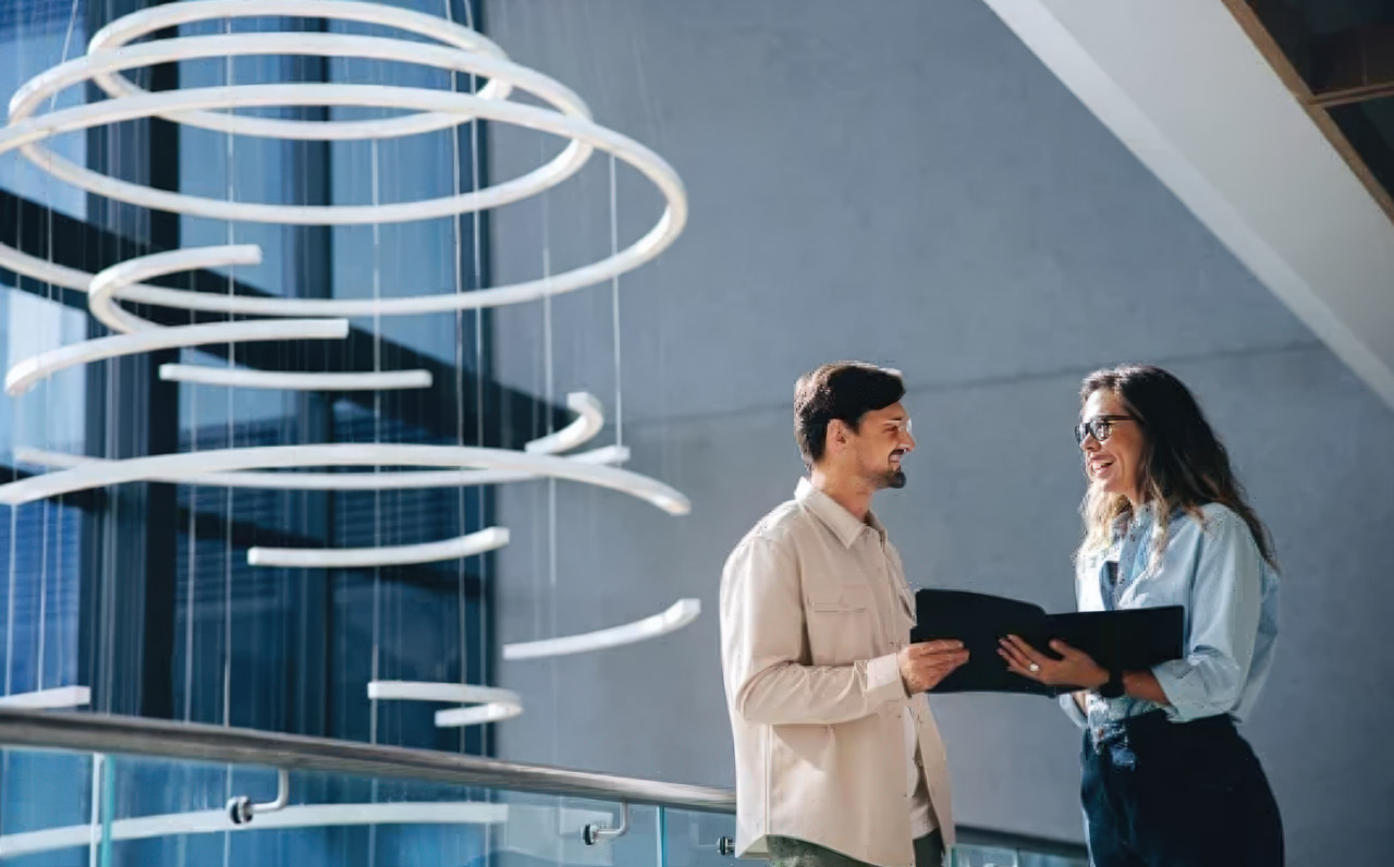 Two professionals converse in a modern office building with distinctive spiral sculpture and glass walls, representing corporate identity and business establishment.