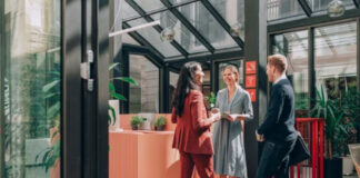 Get More Customers Through Your Door Business professionals meet at a contemporary reception desk in a glass-roofed lobby, demonstrating the welcoming atmosphere that attracts customers to commercial spaces.