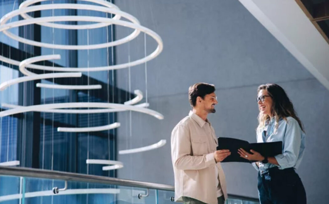 Business professionals collaborate in modern workspace, illustrating evolution of digital business directories and AI search Two business professionals review information on a tablet in a contemporary office with spiral sculpture, representing modern approaches to business directories and digital search.