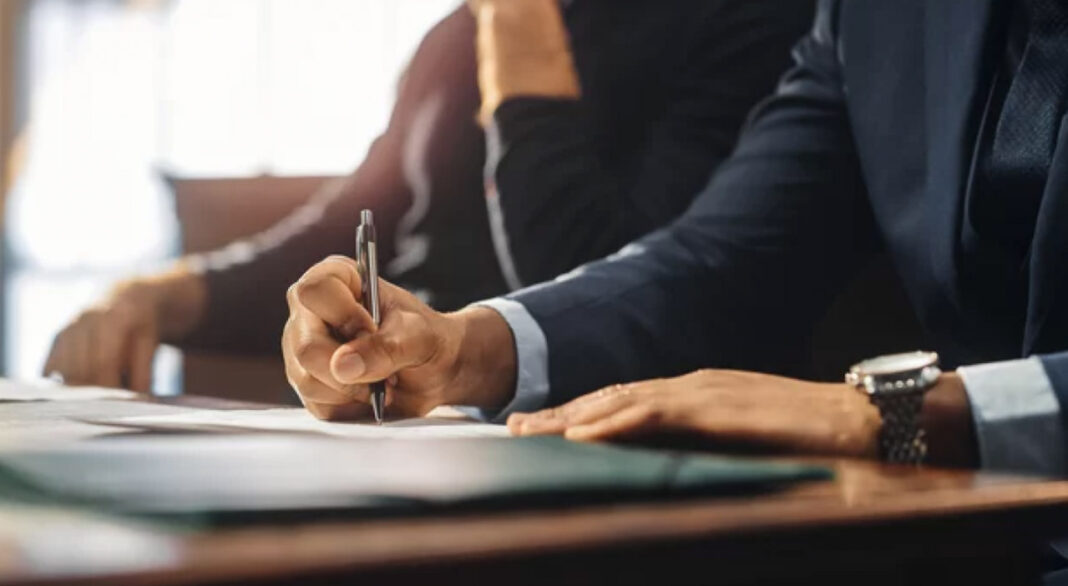 Professional collaboration symbolizes the trust and accuracy essential to quality business directory listings Two business professionals in suits review and sign documents at an office desk, representing the careful attention to detail required for maintaining accurate business directory listings.